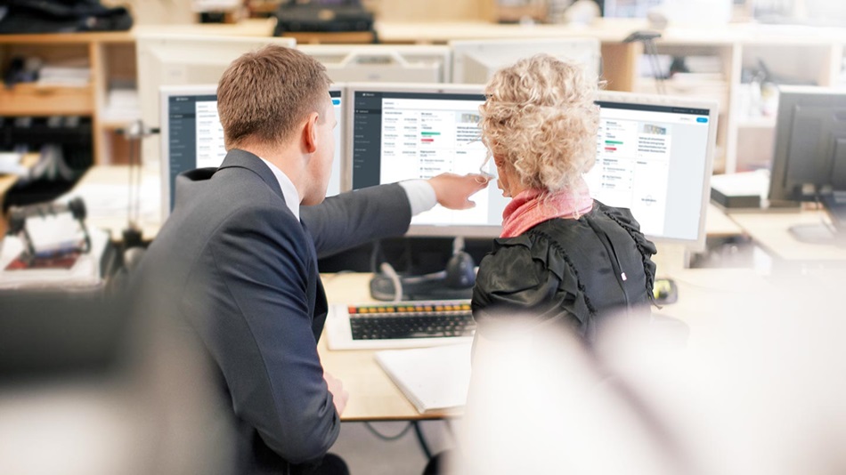 Mann og kvinne sitter i kontorlandskap og ser på skjerm